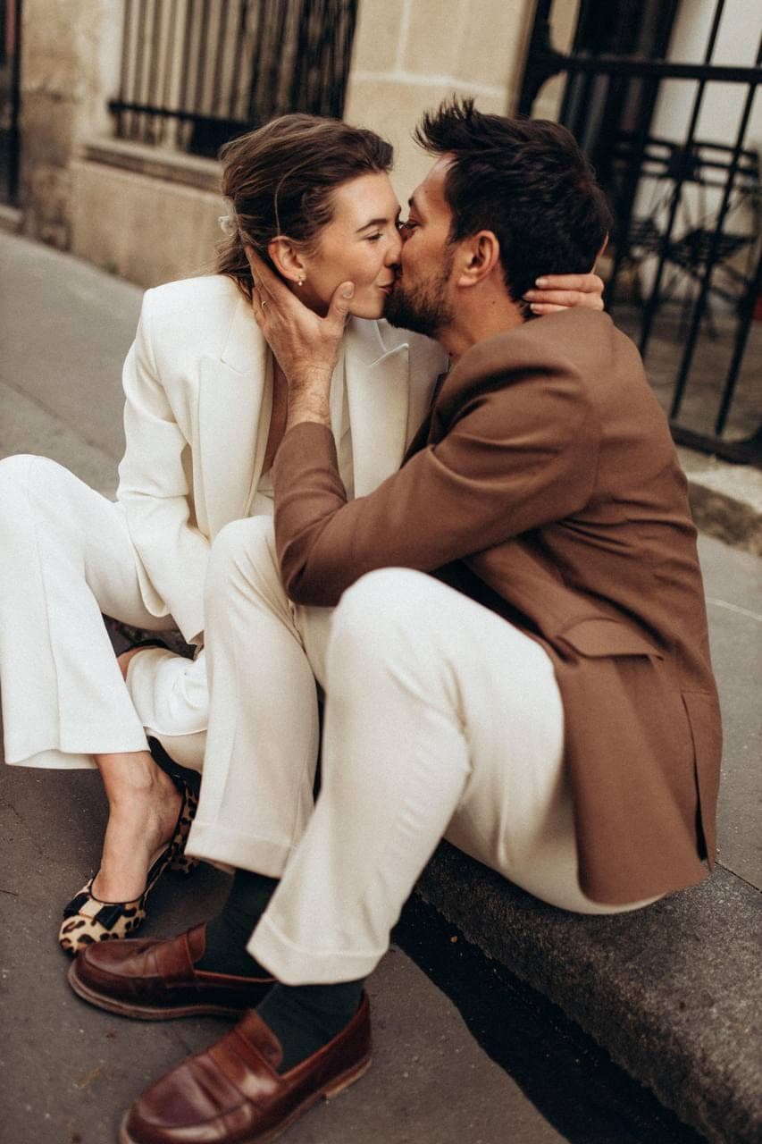Un couple s'embrasse sur une bordure de trottoir parisien.