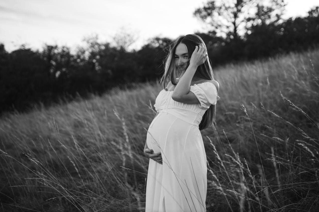 Portrait d'une future maman dans les hautes herbes, en noir et blanc.