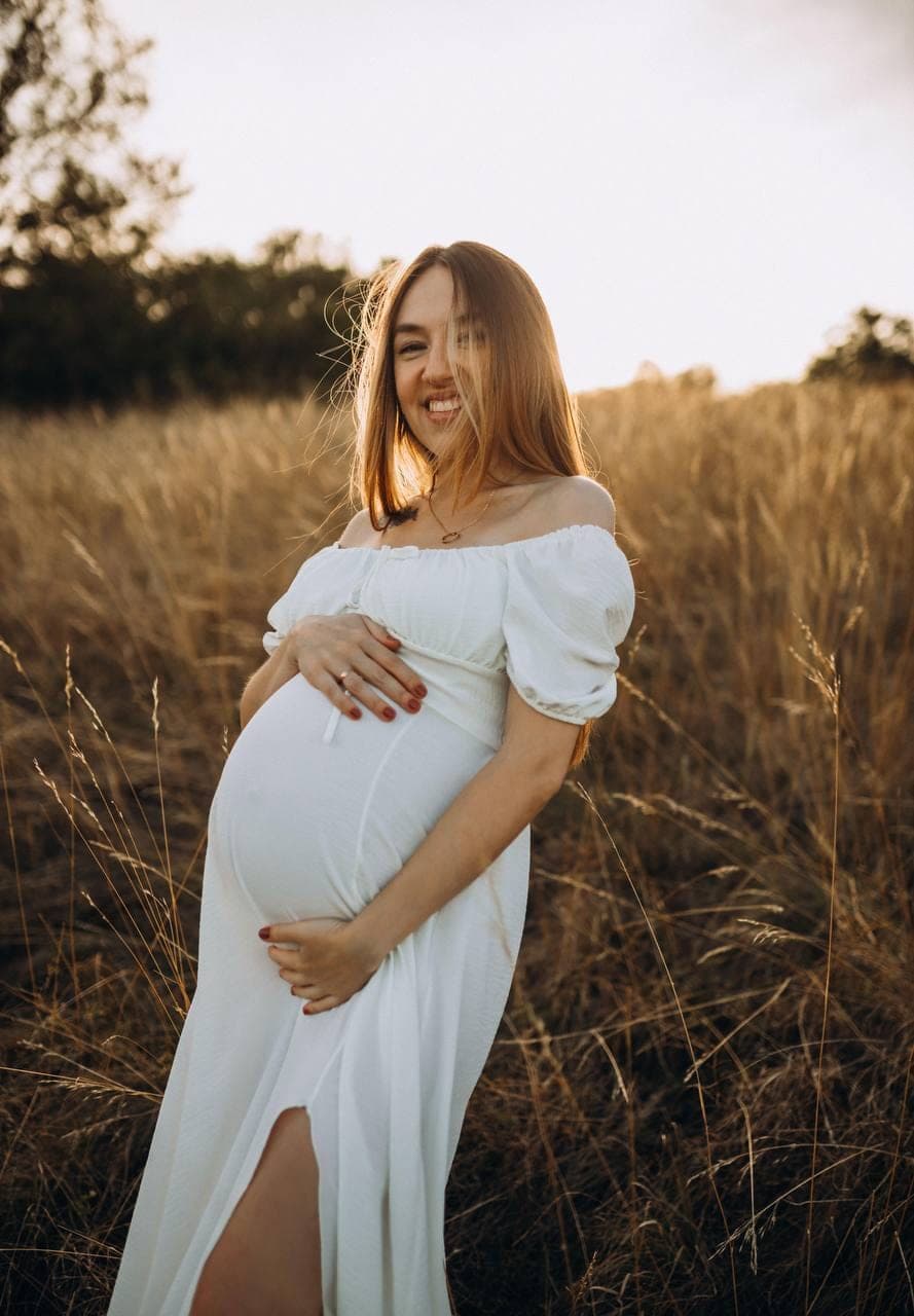 Future maman dans un champ doré, au coucher du soleil.