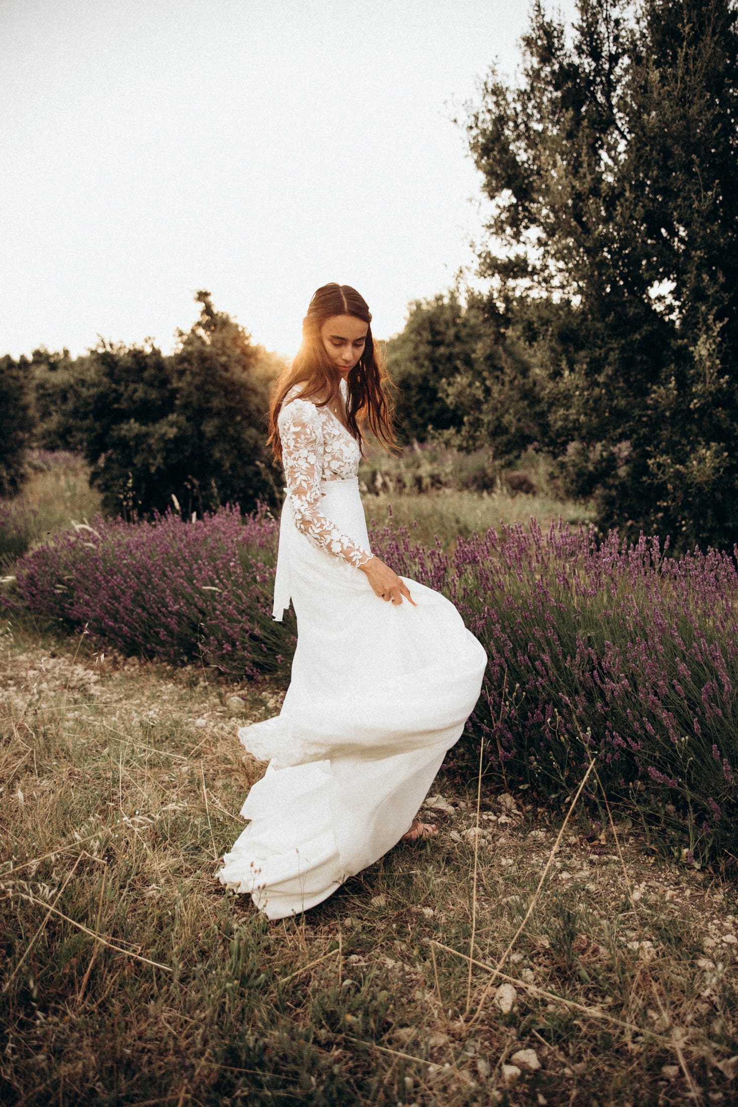 A bride in a lavender field, embroidered dress, eyes lowered.